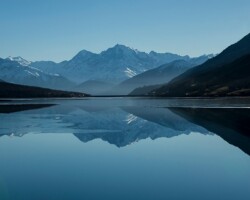 Snow-capped mountains reflected in a calm alpine lake Mountain lake reflecting snow-capped peaks under blue sky