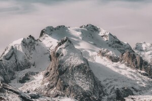 Snow-covered mountain range under cloudy sky Snowy mountain peaks with cloudy sky